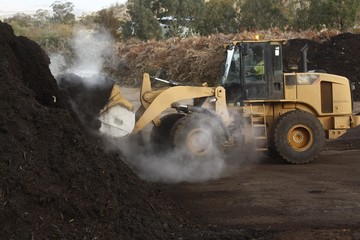 large industrial machinery being used at a garbage dump mixing and excavating green waste mulching...