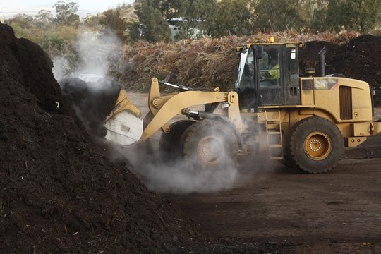 large industrial machinery being used at a garbage dump mixing and excavating green waste mulching it into compost in rural New South Wales, Australia
