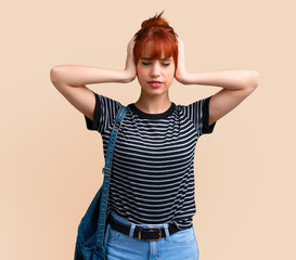 Young student redhead girl covering both ears with hands on ocher background