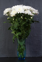 A bouquet of white chrysanthemums in a flower vase over a dark