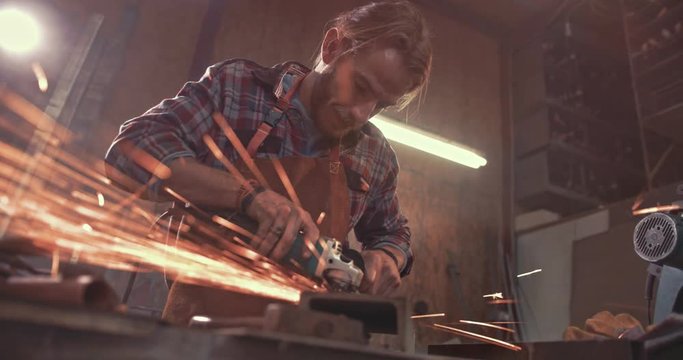 Craftsman working with metal in factory using angle grinder