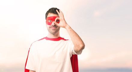 Superhero man with mask and red cape makes funny and crazy face emotion on a sunset background