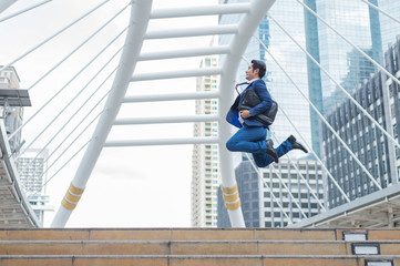 Asian businessman in formal wear holding briefcase while running and jump in the city on a background of building. late for work concept