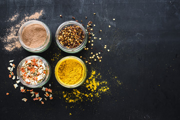 Different spices in glass and food ingredients scattered on black background