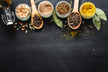 Different spices in glass and food ingredients scattered on black background