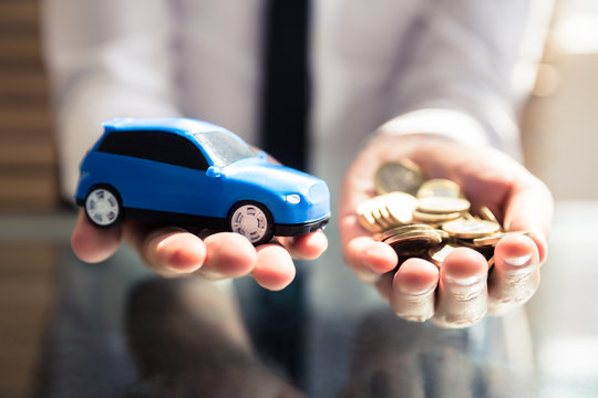 Businessperson Holding Small Blue Car And Golden Coins