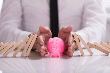 Human Hand Protecting Piggybank From Falling Wooden Blocks