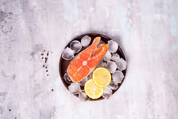 Salmon steaks on ice with lemon slice on wooden plate