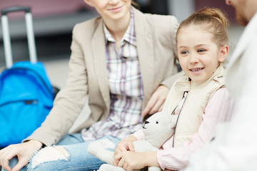 Little girl talking to her dad and mom in airport lounge before departure