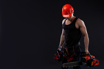 Chainsaw and young worker. The naked man broke the chainsaw. Attractive guy with tool on black...