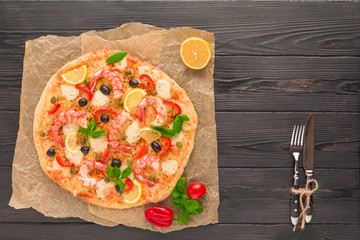 Pizza with prawns, mozzarella cheese, bell pepper and black olives on a rustic wooden table