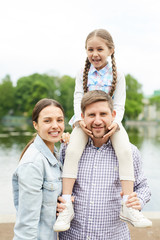 Fototapeta premium Young family in casualwear having promenade in park by waterside on summer day