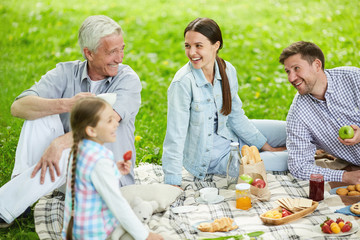 Young couple and mature man laughing during summer picnic with little girl near by