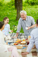 Happy senior man, his granddaughter and young couple enjoying picnic on summer day in park