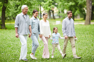 Fototapeta premium Senior and young couples and little girl walking down green glade in park on summer day