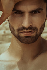 Obraz premium Strong face male model on the nature background with sand and water on the beach on the sunset