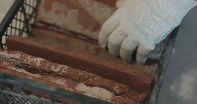 Slow motion pan closeup worker taking brick cuts tile from container
