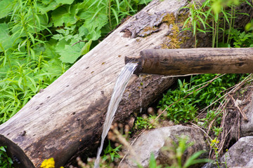 Mountain water spring out of wooden gutter from rocky creek