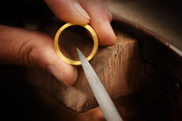 goldsmith hand holds a golden ring and works on it with a metal file, close up with copy space, ...