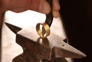 hand of a goldsmith punches a hallmark into a golden ring on an anvil, close up with copy space