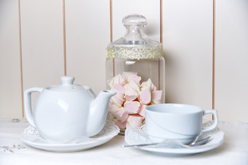 A glass jar of marshmallow stands behind a kettle and a cup on a saucer with lace.
