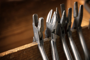 different pliers from a goldsmith on a wooden tool holder on the jewelry workplace, copy space