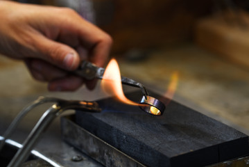hand of a goldsmith holds a golden ring with tweezers in a gas flame to glow it, copy space in the...