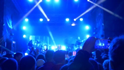 night entertainment, admirer shoot on telephone performing of rock band on brightly lit stage