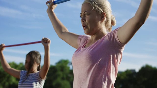 Adult serious woman and children doing exercise with fitness stick on field in summer sunlight