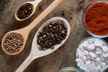 Various spices in wooden spoons and bowls and some salt on an old wooden barrel, top view, close-up, selective focus.