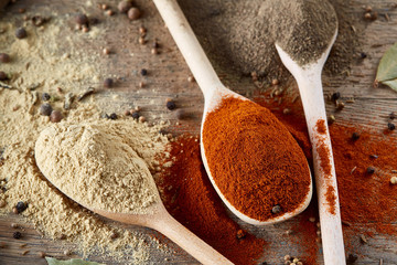 Top view of a wooden spoons full of paprica and black pepper on wooden barrel background, selective focus.