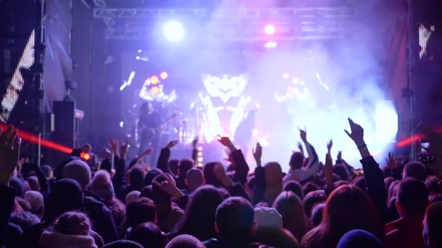 jumping fans with hands up delight of live music of rock band on bright scene in slow motion