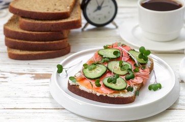 Rye sandwich with salmon, cucumber, cheese cream and micro greens.   Tasty and healthy Breakfast on the table.