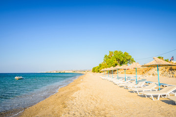 Fototapeta na wymiar Beaches, Greece, Kos Island, Kardamena: beautiful holiday setting on a secluded beach with umbrellas on the Greek Aegean Sea with turquoise waters and a picturesque bay and islands in the background