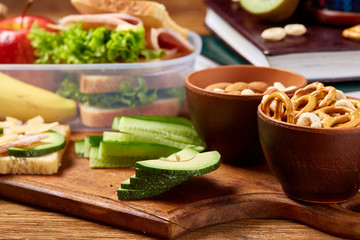 School or picnic lunch box with sandwich and various colorful vegetables and fruits on wooden background, close up.