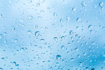 Drops of rain on blue glass background. The sky with clouds on background.