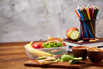 School or picnic lunch box with sandwich and various colorful vegetables and fruits on wooden background, close up.