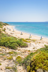 Fototapeta na wymiar Beaches, Greece, Kos Island, Cap Helona: beautiful holiday setting on a secluded beach with umbrellas on the Greek Aegean Sea with turquoise waters and a picturesque bay and islands in the background