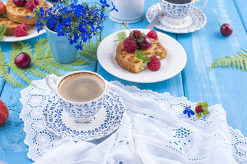 Small cupcakes with berries, strawberries and cherries. Delicious sweet breakfast and fragrant coffee, on a blue wooden background and flowers. Copy space