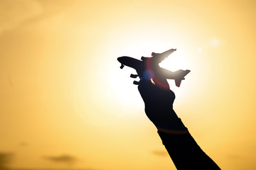 Silhouette of Hand holding airplane model on Colorful dramatic sky at Sunset