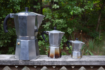 Family of new and used stovetop espresso machines in the moka style outside on a railing of wood.