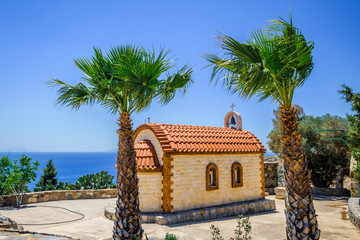 Church, Greece, Kos Island: old cozy little orange stone church with red roof chapel in traditional colors which perched on the greeksy sea next to a small tree over the barren mountains - Powered by Adobe