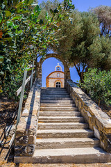 Fototapeta na wymiar Church, Greece, Kos Island: old cozy little orange stone church with red roof chapel in traditional colors which perched on the greeksy sea next to a small tree over the barren mountains