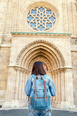 Fototapeta na wymiar rear view of a tourist woman with backpack looking at historical architecture of a catholic gothic church, sightseeing trip concept