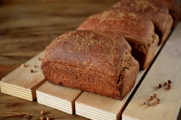 Loaves of rye bread sprinkled with coriander on a wooden board