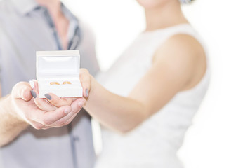Fototapeta na wymiar Defocused portrait of young coulpe bride and groom holding golden wedding or engagement rings in small white gift box on white background. Copy space