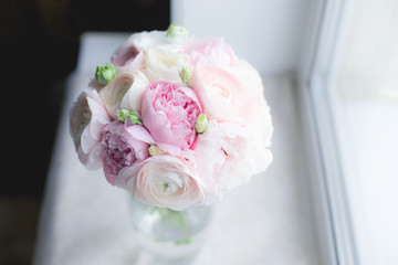 Gorgeous bridal bouquet of pink peonies Sarah Bernhardt, ranunculuses Hanoi, garden roses and white Eustoma in a vase on the window background. Wedding floristry