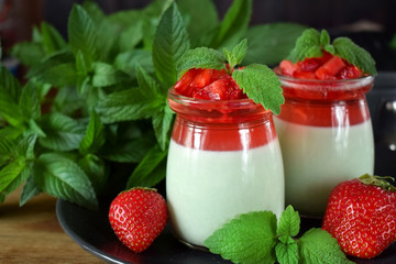 Two layered panna cotta with matcha tea topped with strawberry jelly, berries and mint in glass jars