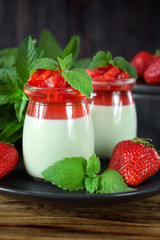 Two layered panna cotta with matcha tea topped with strawberry jelly, berries and mint in glass jars