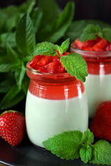 Two layered panna cotta with matcha tea topped with strawberry jelly, berries and mint in glass jars